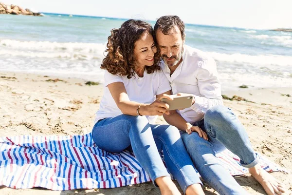 中年时 他那对惊慌失措的夫妇坐在沙滩上的毛巾上 靠智能手机度日 — 图库照片