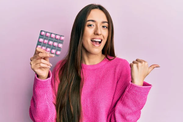 Menina Hispânica Jovem Segurando Pílulas Apontando Polegar Até Lado Sorrindo — Fotografia de Stock