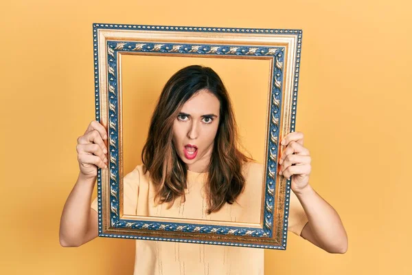 Young Hispanic Girl Holding Empty Frame Shock Face Looking Skeptical — Stock fotografie