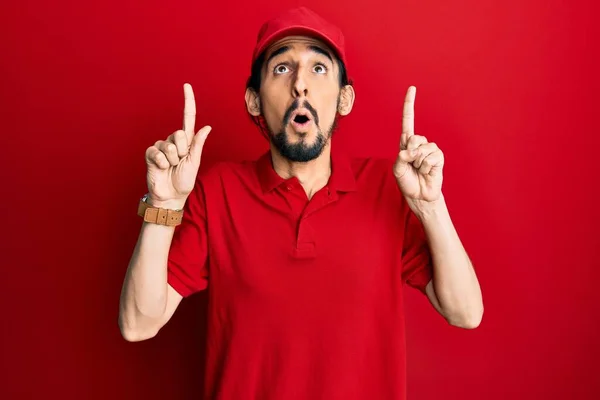 Young Hispanic Man Wearing Delivery Uniform Cap Amazed Surprised Looking — Stock fotografie
