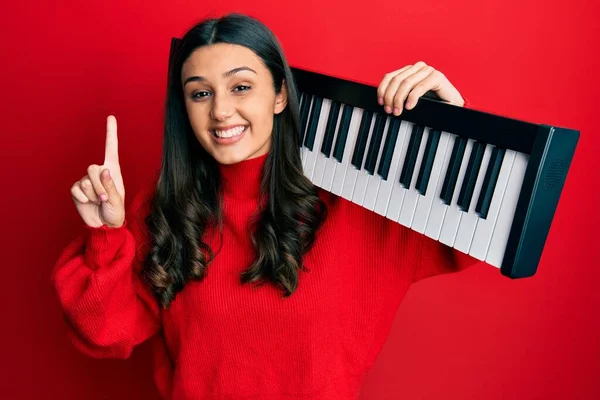 Young Hispanic Woman Holding Piano Keyboard Smiling Idea Question Pointing — Stockfoto