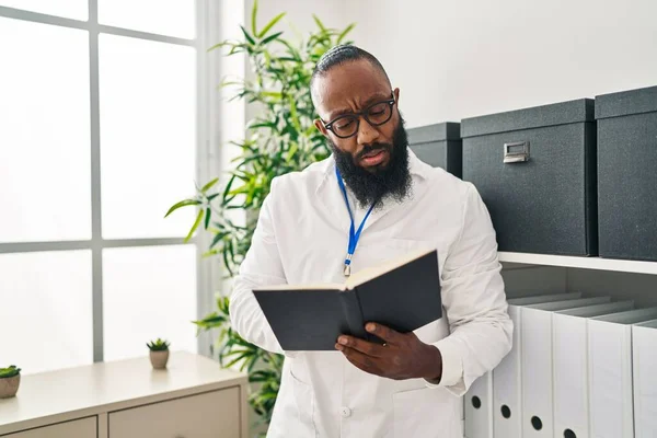 Young African American Man Wearing Doctor Uniform Reading Book Clinic — Stockfoto