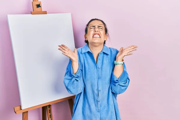 Young Hispanic Woman Standing Painter Easel Stand Celebrating Mad Crazy — ストック写真