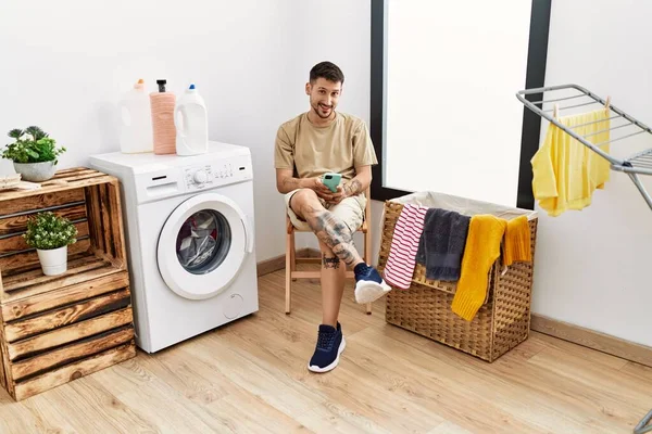 Young Hispanic Man Waiting Washing Machine Using Smartphone Laundry Room — Stockfoto