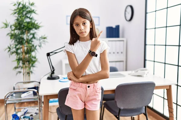 Young Hispanic Girl Standing Pediatrician Clinic Pointing Hand Finger Side — Stockfoto
