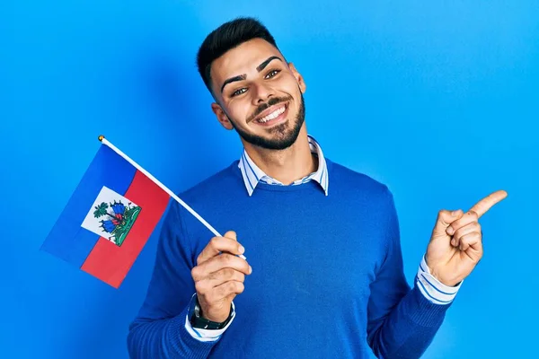Joven Hispano Con Barba Sosteniendo Bandera Haití Sonriendo Feliz Señalando —  Fotos de Stock