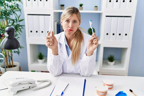 Beautiful Dentist Woman Holding Ordinary Toothbrush Electric Toothbrush Skeptic Nervous — Stockfoto