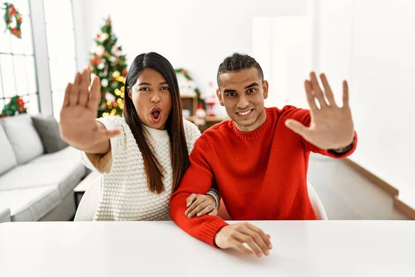 Young Latin Couple Sitting Table Christmas Tree Doing Stop Gesture — Stockfoto