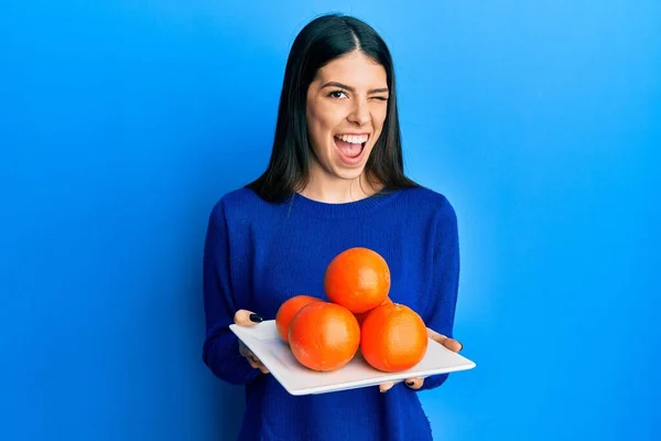 Young Hispanic Woman Holding Plate Fresh Oranges Winking Looking Camera — Foto Stock