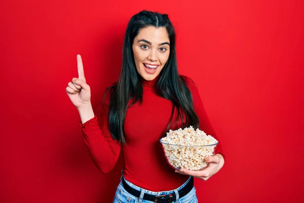 Young Hispanic Girl Eating Popcorn Smiling Idea Question Pointing Finger — 스톡 사진