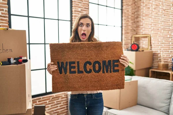 Young Woman Holding Welcome Doormat New Home Afraid Shocked Surprise – stockfoto