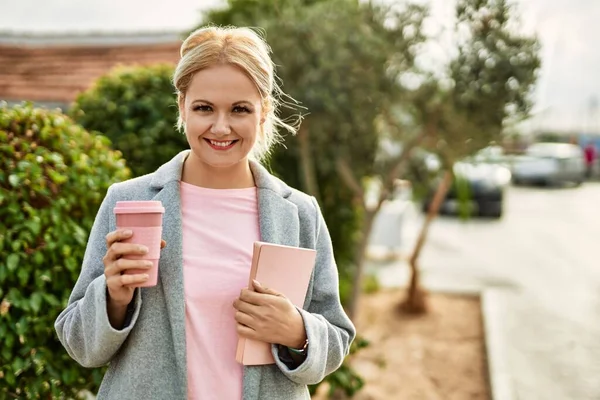 Genç sarışın iş kadını gülümseyerek şehirde kahve içiyor..