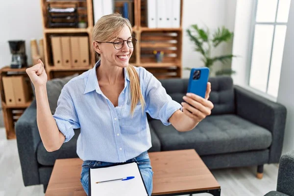 Beautiful woman doing online therapy session at consultation office screaming proud, celebrating victory and success very excited with raised arm 