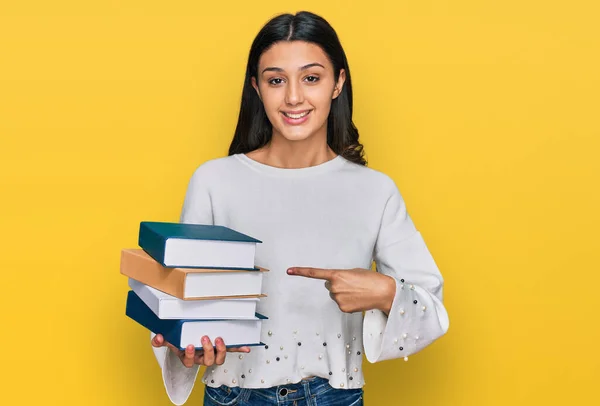 Young Hispanic Girl Holding Pile Books Smiling Happy Pointing Hand — 스톡 사진