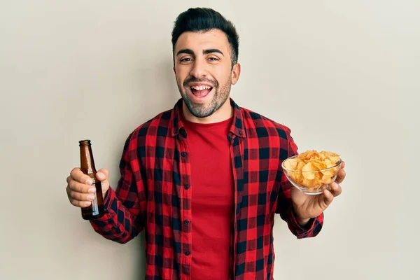 Young Hispanic Man Drinking Bottle Beer Eating Chip Potatoes Smiling — Foto de Stock