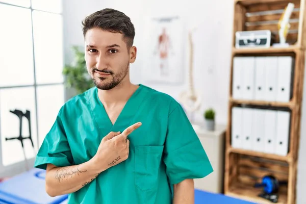 Young Physiotherapist Man Working Pain Recovery Clinic Pointing Aside Worried — Stockfoto
