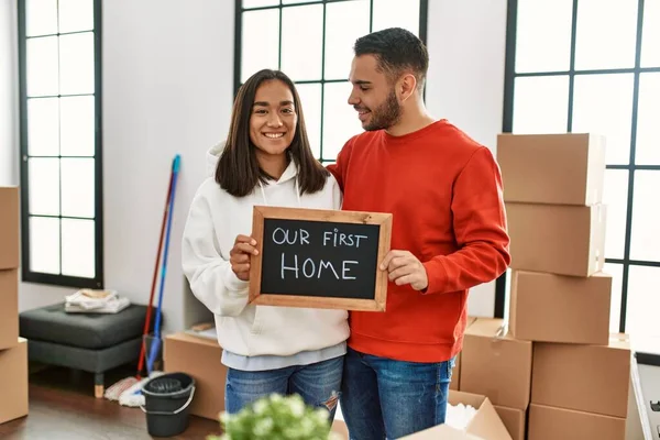Genç Latin çift mutlu bir şekilde gülümsüyor. İlk ev mesajımızla birlikte ellerinde tahtayla..