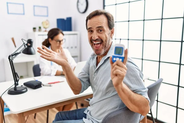 Middle Age Man Doctor Clinic Holding Glucose Meter Device Celebrating — Zdjęcie stockowe