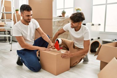 İki İspanyol erkek gülümsüyor. Yeni evlerinde kendilerine güvenen karton kutuları var.