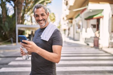Orta yaşlı İspanyol adam spor giyer. Sokakta akıllı telefon kullanır.