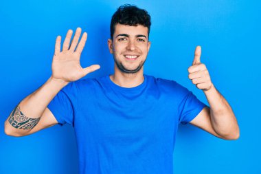 Young hispanic man wearing casual blue t shirt showing and pointing up with fingers number six while smiling confident and happy. 