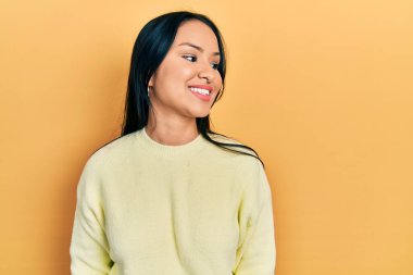 Beautiful hispanic woman with nose piercing wearing casual yellow sweater looking to side, relax profile pose with natural face and confident smile. 
