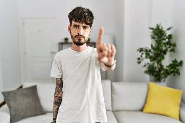 Hispanic man with beard at the living room at home pointing with finger up and angry expression, showing no gesture 
