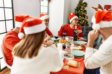 Bir grup genç, mutlu bir şekilde gülümseyerek evde Noel yemeği yiyor..
