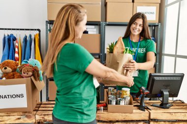 Anne ve kızı gönüllü üniforması giyip hayır kurumunda poşet taşıyorlar.