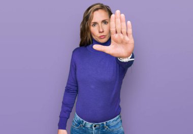 Sıradan kıyafetler giyen genç sarışın kadın avuç içiyle şarkı söylemeyi kesiyor. Yüzünde olumsuz ve ciddi bir jest olan uyarı ifadesi. 