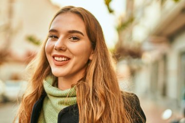 Genç sarışın kız gülümsüyor, mutlu bir şekilde şehirde duruyor..