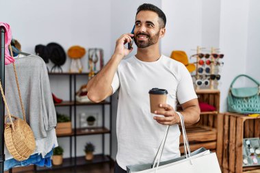 Young hispanic man customer talking on the smartphone shopping at clothing store