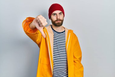 Sakallı, sarı yağmurluk giyen, mutsuz görünen, reddedilmiş ve olumsuz davranan beyaz bir adam. kötü ifade. 