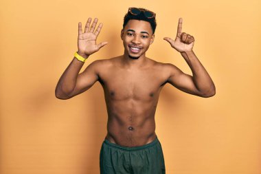 Young african american man wearing swimwear and swimmer glasses showing and pointing up with fingers number seven while smiling confident and happy. 