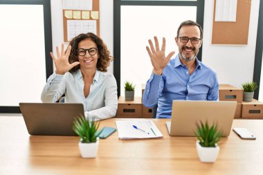 Middle age hispanic woman and man sitting with laptop at the office showing and pointing up with fingers number ten while smiling confident and happy. 