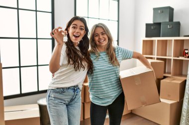 Mutlu bir şekilde gülümseyen genç çift yeni evin anahtarını ve karton kutuyu tutuyor..