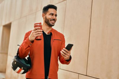 Genç İspanyol adam akıllı telefon kullanıyor. Şehirde kahve kaskı içiyor..