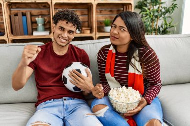 Evdeki kanepede oturan genç latin çift futbol maçını izliyor ve destekliyor..