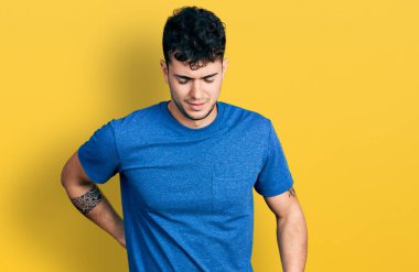 Sırt ağrısı çeken, eli ile dokunan, kaslı, sıradan tişörtler giyen İspanyol genç bir adam. 