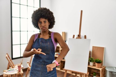 Young african american woman with afro hair at art studio in hurry pointing to watch time, impatience, upset and angry for deadline delay 
