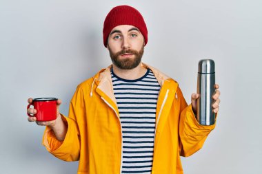 Kafkas sakallı, elinde bir fincan kahve, termo şüpheci ve gergin bir adam sorun yüzünden surat asıyor. negatif kişi. 