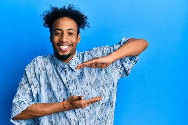 Young african american man with beard wearing casual clothes gesturing with hands showing big and large size sign, measure symbol. smiling looking at the camera. measuring concept. 