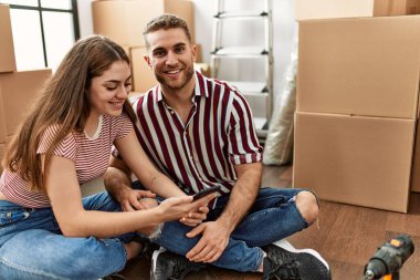 Yeni evimizde akıllı telefon kullanarak mutlu bir şekilde gülümseyen beyaz bir çift..