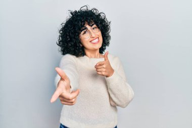 Young middle east woman wearing casual white tshirt pointing fingers to camera with happy and funny face. good energy and vibes. 