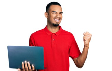 Young african american man working using computer laptop screaming proud, celebrating victory and success very excited with raised arms 