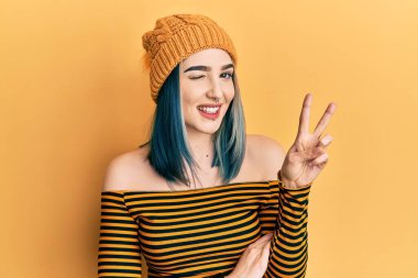 Young modern girl wearing wool hat smiling with happy face winking at the camera doing victory sign. number two. 