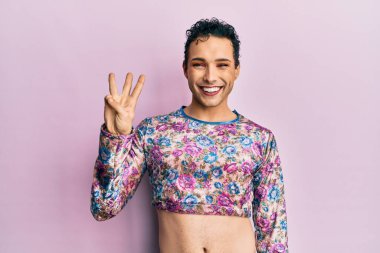 Handsome man wearing make up wearing fashion clothes showing and pointing up with fingers number three while smiling confident and happy. 