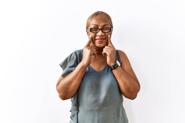 Mature hispanic woman wearing glasses standing over isolated background smiling with open mouth, fingers pointing and forcing cheerful smile 