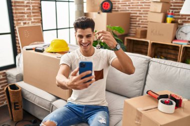 Young hispanic man having video call holding key of house at new home