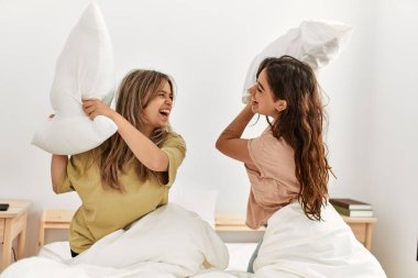 Mutlu gülümseyen genç çift evdeki yatakta yastıklarla kavga ediyor..